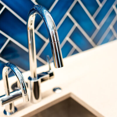 New modern faucet and kitchen sink closeup with countertop, blue vibrant backsplash and shiny clean stainless steel handle